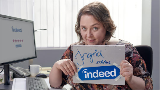 Ingrid hält ein Schild hoch, auf dem steht: "Ingrid erklärt indeed"